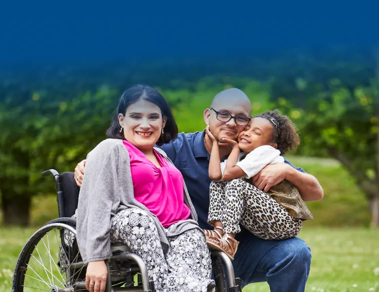 Family of three smiling together outdoors, woman in wheelchair